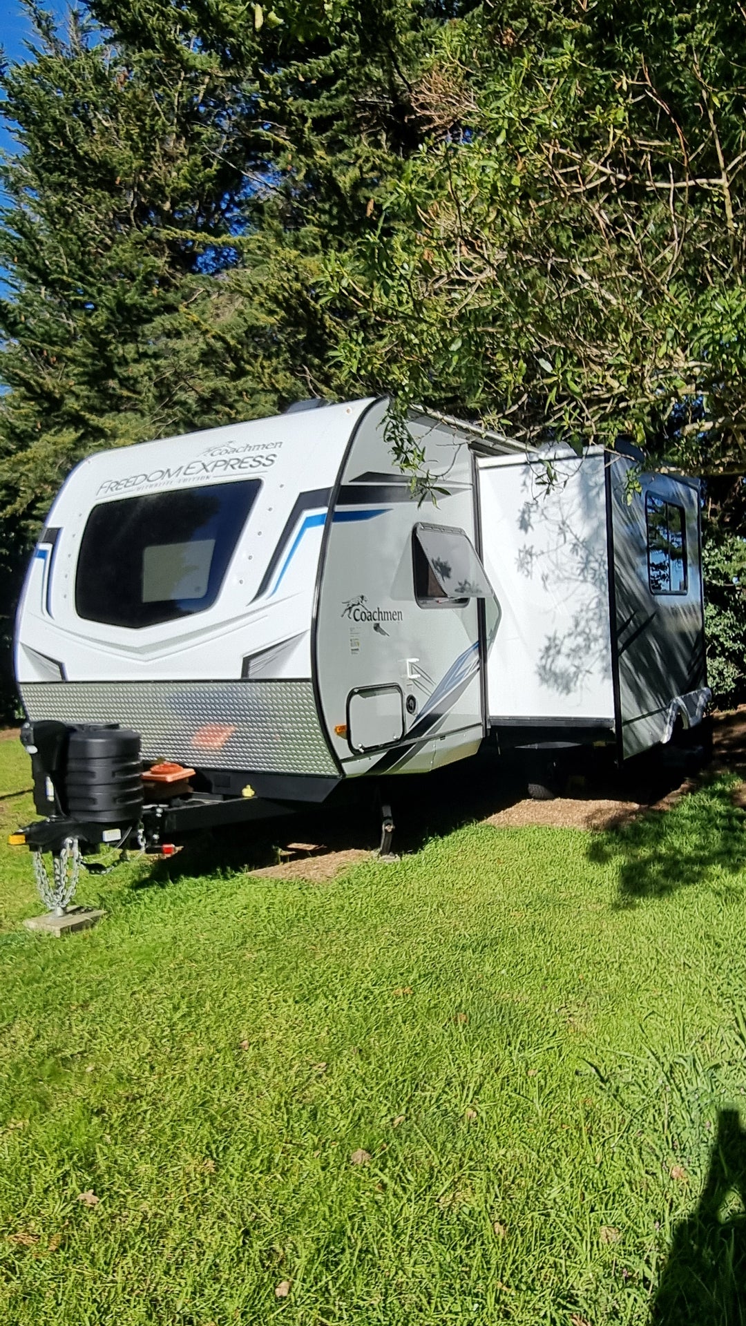 Top-down view of a white and black RV parked on grass with trees in the background