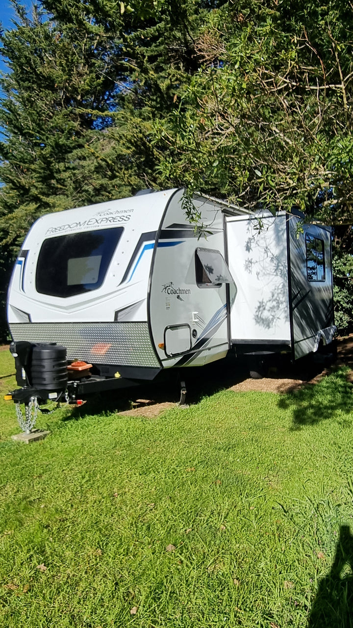 Top-down view of a white and black RV parked on grass with trees in the background