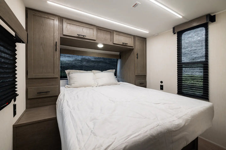 Compact bedroom with a bed, cabinets, and windows in a small living space.