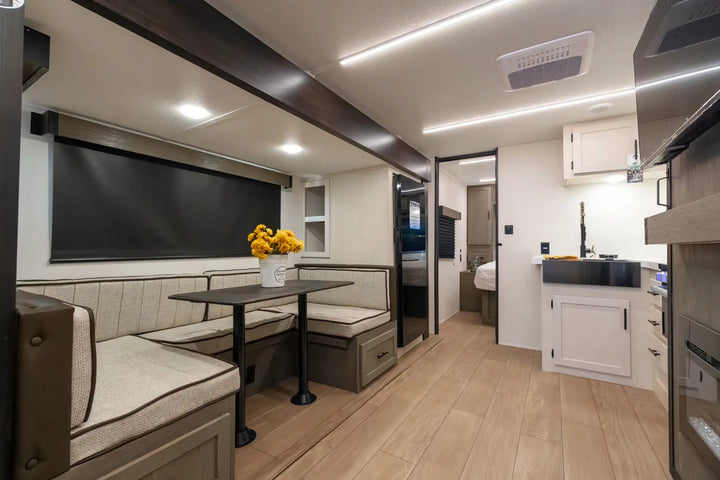 Modern kitchen and dining area inside a vehicle with wooden flooring and neutral color scheme.