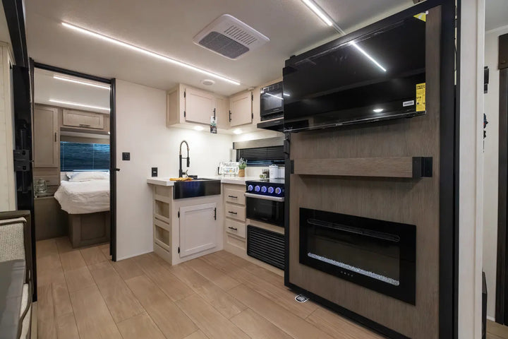 Modern kitchen and living area inside a vehicle with a TV mounted on the wall.