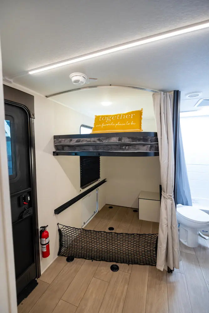 Compact living space with a small bed, storage basket, and wall-mounted shelf.