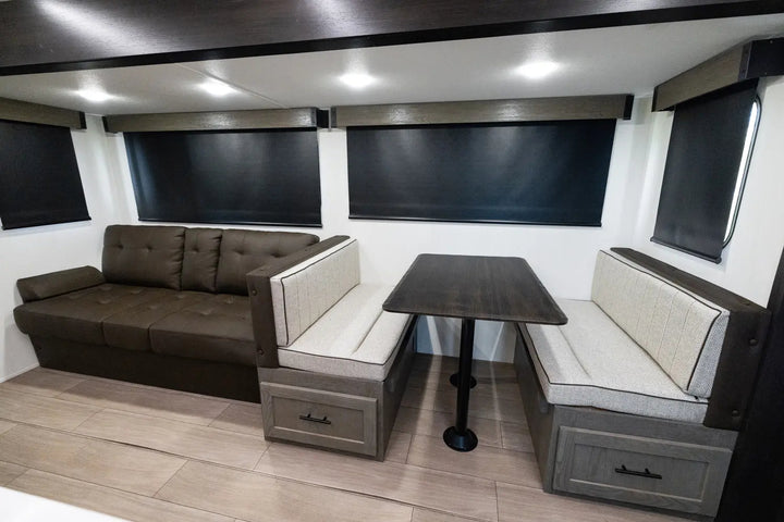 Interior of a modern vehicle with a brown sectional sofa, table, and storage drawers.
