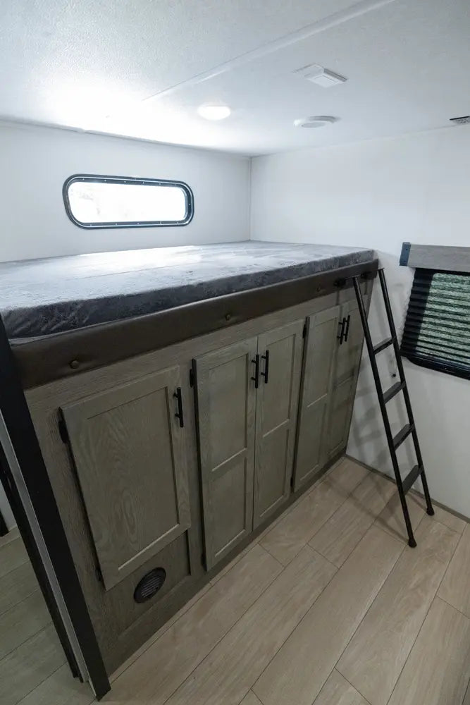 Compact living space with a bed, cabinets, and a ladder inside a vehicle or small home.