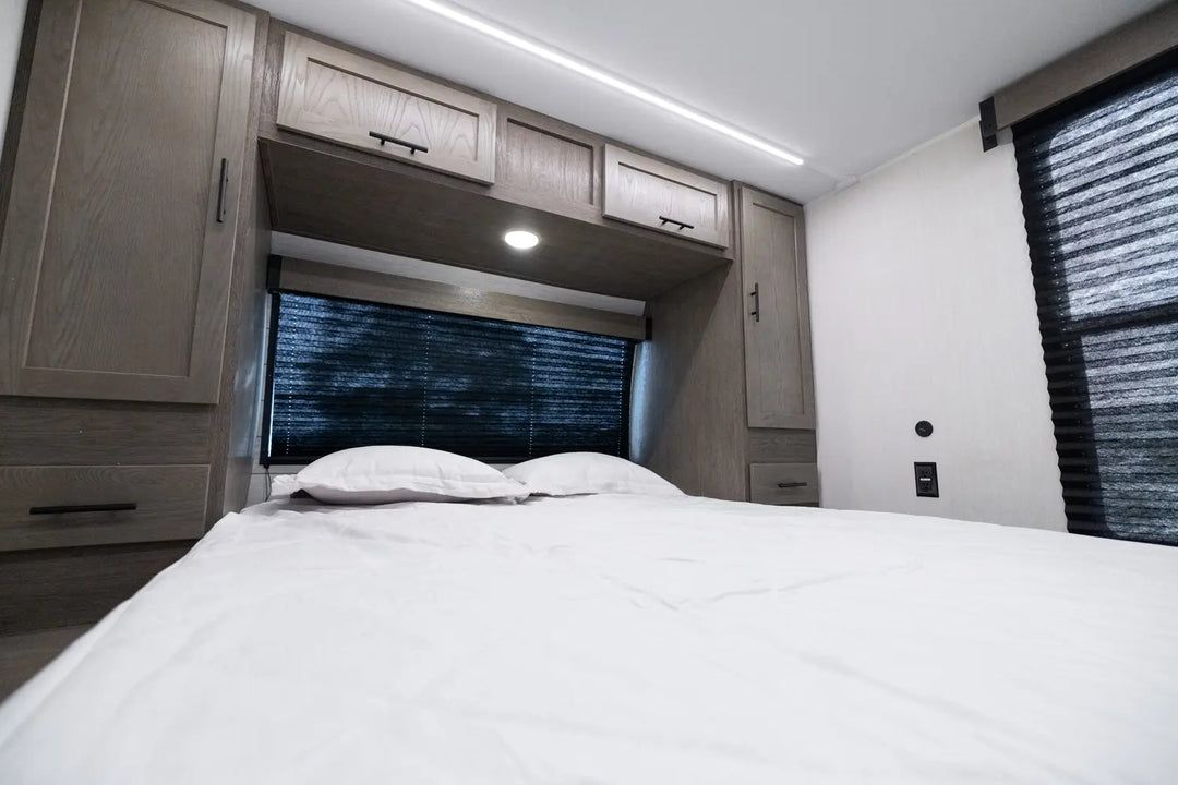 Bedroom interior of a vehicle with bed, cabinets, and windows.