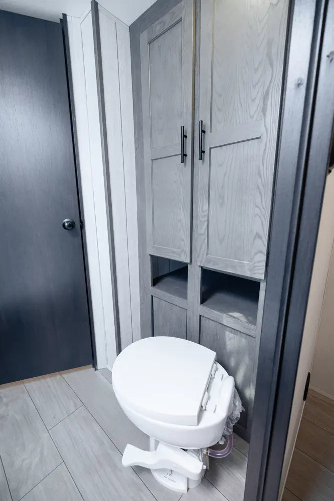 White toilet in a bathroom with gray cabinets and a dark door.