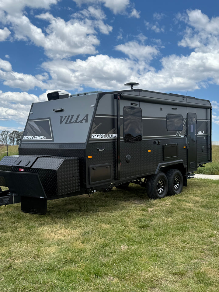 Black Villa trailer parked on grass with a blue sky and clouds in the background