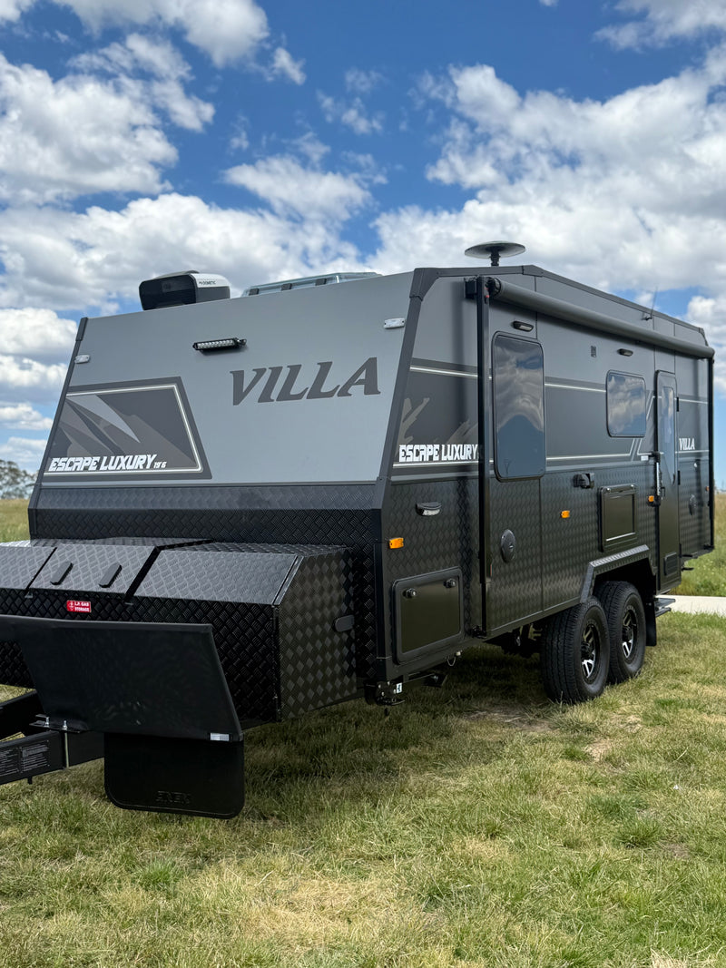 Black Villa travel trailer parked on grass with a blue sky background