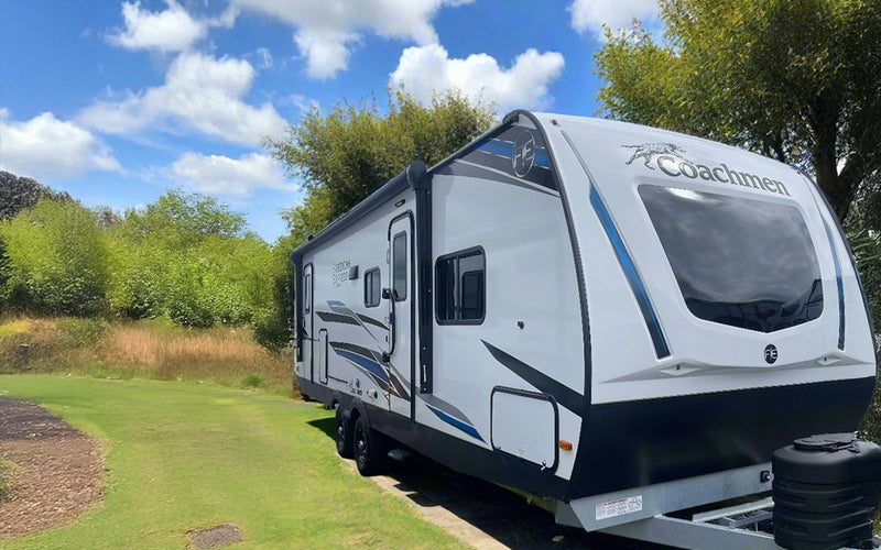 A white and gray Freedom Express bunkhouse travel trailer with exterior kitchen and awning, parked on grass.