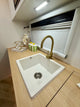 White kitchen sink with gold faucet on a wooden countertop.