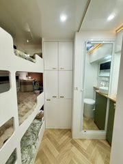 Small living space with bunk beds, cabinets, and a bathroom reflection in a mirror.