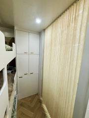 Children's room with bunk bed, white wardrobe, and beige curtain.