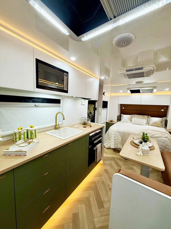 Modern kitchen and bedroom interior with olive green cabinets, white appliances, and wooden flooring.