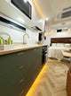Modern kitchen with olive green cabinets and a bed in the background