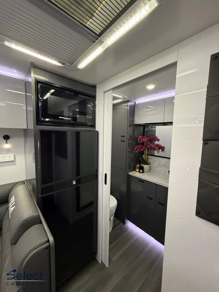 Modern interior of a caravan with gray seats, black cabinets, and a small kitchen area.