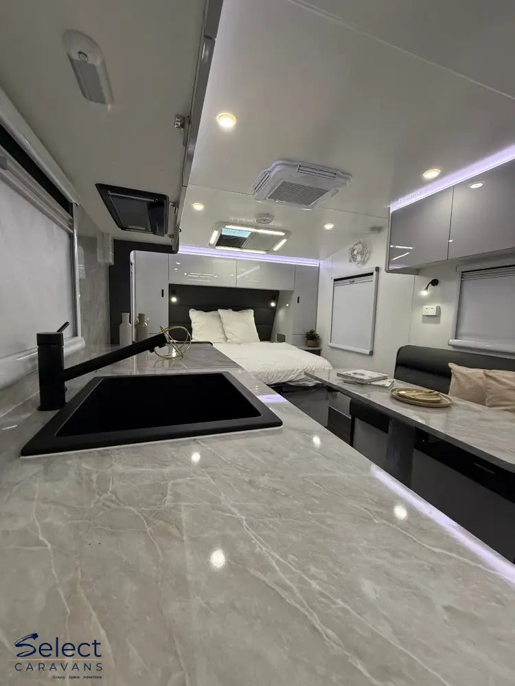 Modern kitchen area inside a caravan with marble countertop, sink, and bed in the background.
