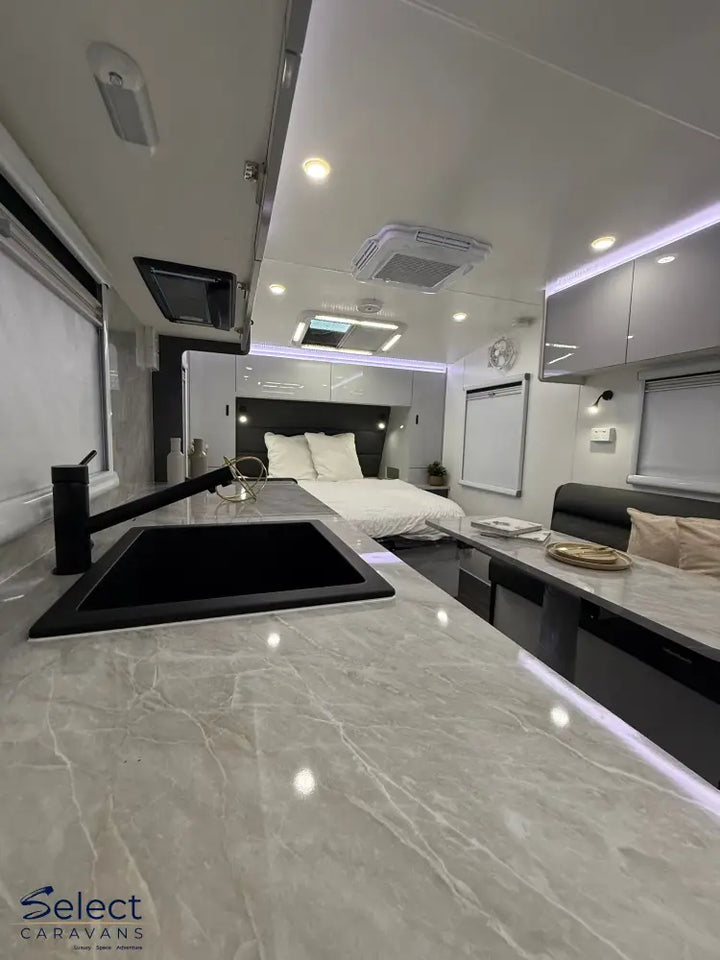 Modern kitchen area inside a caravan with marble countertop, sink, and bed in the background.