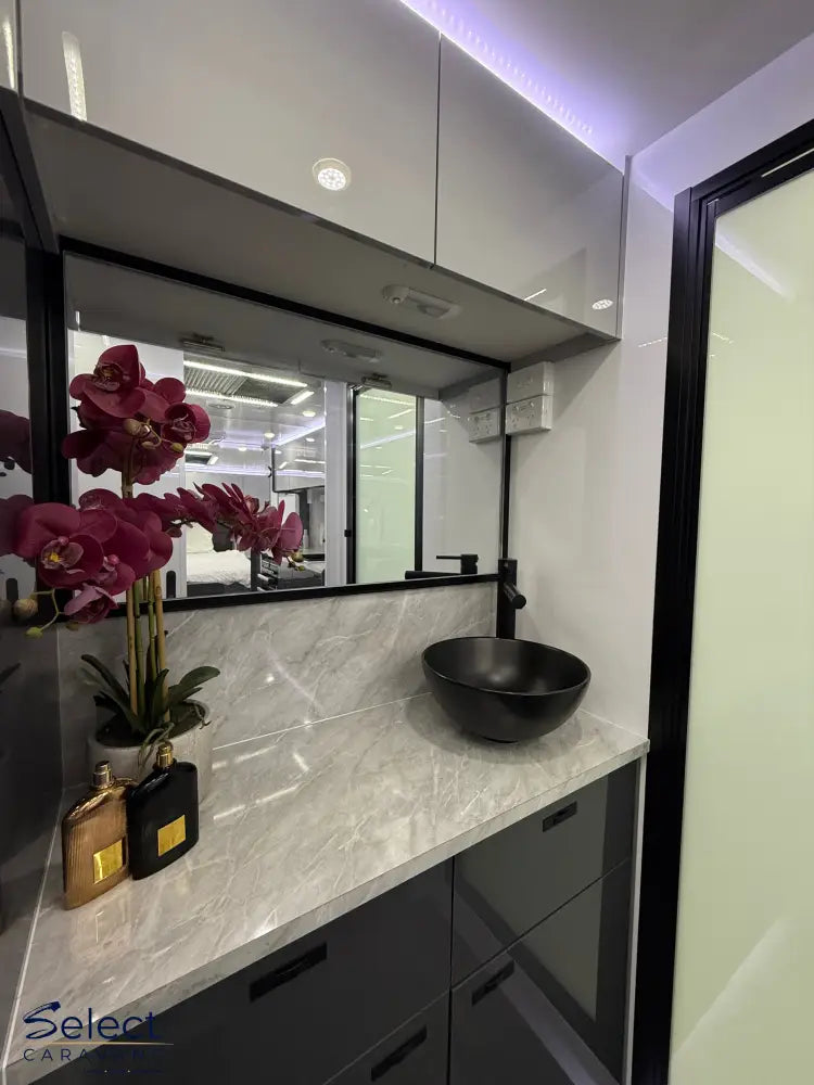 Bathroom vanity with marble countertop, black bowl, and orchids.
