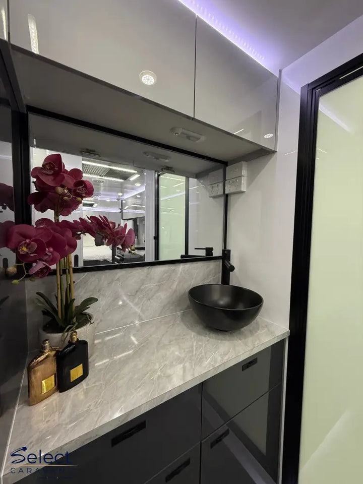 Bathroom vanity with marble countertop, black bowl, and orchids.