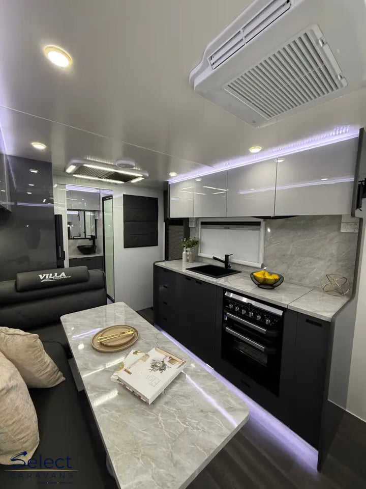 Modern kitchen and living area inside a vehicle with marble countertops and black appliances.