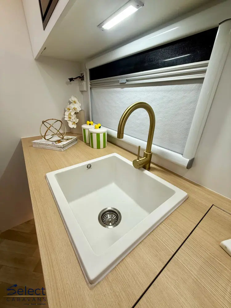 White kitchen sink with gold faucet on a wooden countertop.