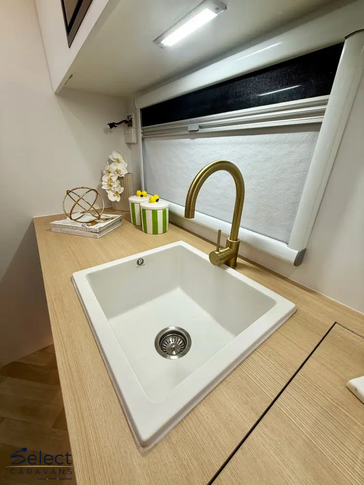 White kitchen sink with gold faucet on a wooden countertop.