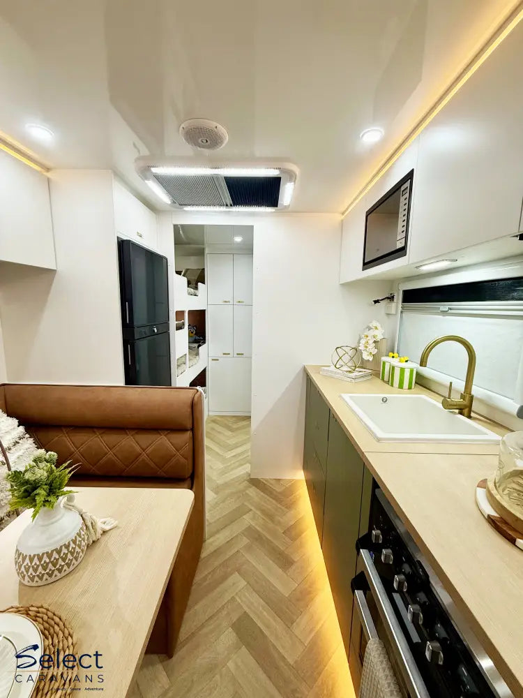Modern kitchen and living area inside a vehicle with wooden floor and white walls.